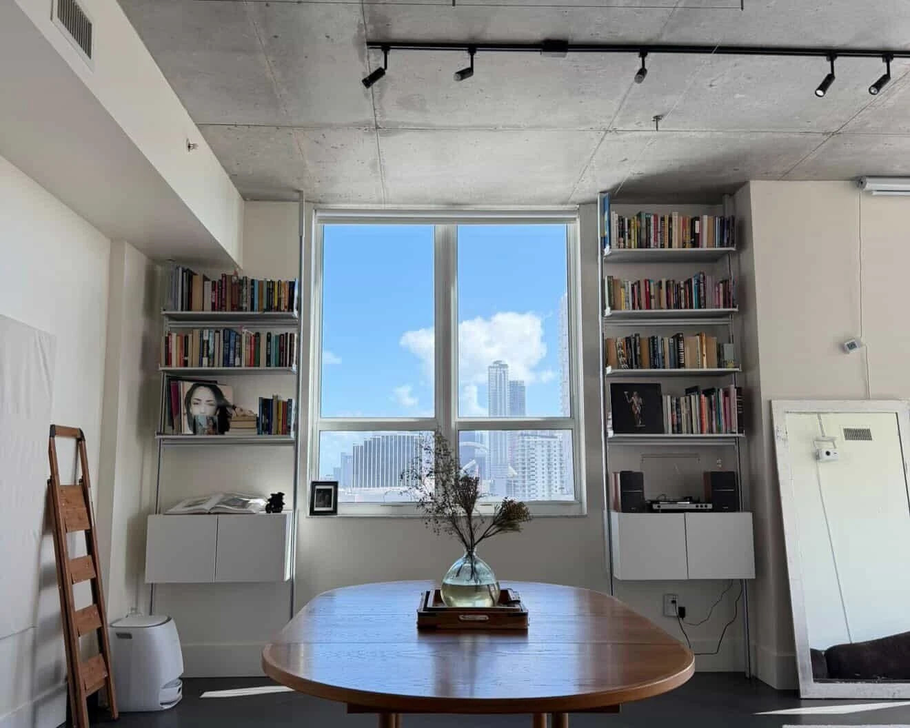 Modern living room with bookshelves, a table, and a large window view.